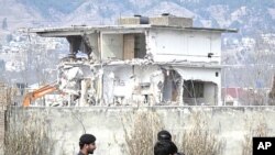 Policemen and residents stand near while demolition work is carried out on the building where al Qaeda leader Osama bin Laden was killed by U.S. special forces last May, in Abbottabad, February 26, 2012.