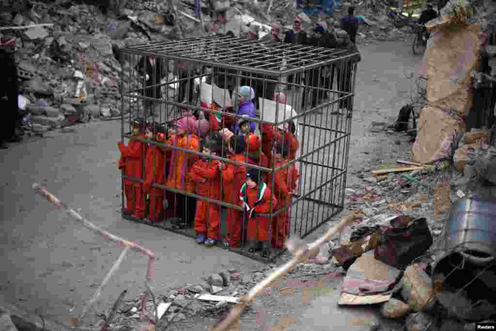 Children wearing orange suits depicting victims of the Islamic State carry banners inside a cage during a protest against forces loyal to Syria&#39;s President Bashar al-Assad, in Douma Eastern Al-Ghouta, near Damascus.