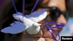 FILE - Jennifer Gordon holds a fabric dove at the base of balloons as she pays tribute to musician Prince at a makeshift memorial outside the fence of Paisley Park, his home and recording studio, in suburban Minneapolis, Minnesota, April 22, 2016.