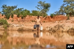 Seorang pria mengambil air dari kolam untuk memberi minum anak sapinya di Matobo, Matabeleland, pada 10 Mei 2024. (Foto: AFP)