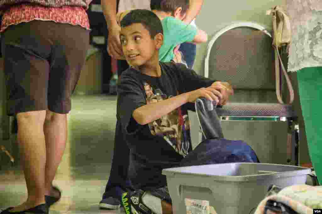 A 12-year-old boy, who arrived with his mother and brothers from Mexico, learns to make their donated clothes fit in a small suitcase at the Holding Institute in Laredo, Texas, Aug. 12, 2014. (VOA / V. Macchi)