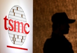 FILE - A security personnel stands near the logo of Taiwan Semiconductor Manufacturing Co. Ltd (TSMC) during an investor conference in Taipei, July 16, 2014.