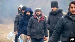 Migrants line up to collect drinking water as they gather at the Belarus-Poland border near Grodno, Belarus, Nov. 12, 2021.