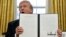 President Donald Trump holds up one of the Section 201 actions that he signed during a ceremony in the Oval Office of the White House in Washington, Jan. 23, 2018. Trump says he is imposing new tariffs to "protect American jobs and American workers." 
