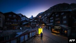 (资料照）2020年3月18日晚上，一行人在疫情期间在瑞士阿尔卑斯山旅游第泽马特的街道上看发光地图板。
