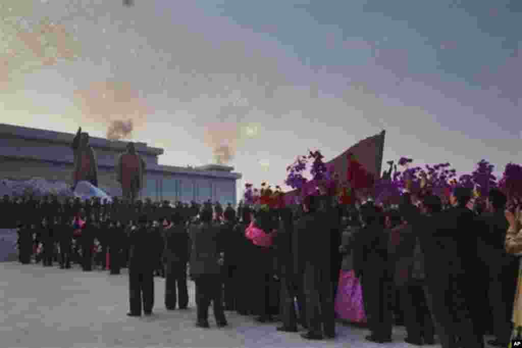 Fireworks explode and North Koreans wave flowers as sheets are pulled from two statues at an unveiling ceremony for statues of the late leaders, Kim Il Sung, left, and Kim Jong Il, in Pyongyang, North Korea, Friday, April 13, 2012. (AP Photo/David Guttenf