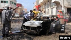 Members of the public and firefighters move the shell of a damaged vehicle after an explosion near the main market in Somalia's capital Mogadishu, July 9, 2013. 