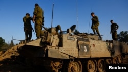 Israeli soldiers stand on top of an Armoured Personnel Carrier (APC) near the border with Gaza