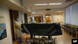 FILE - Hospital staff members enter an elevator with the body of a COVID-19 victim on a gurney at St. Jude Medical Center in Fullerton, Calif., July 7, 2020. 
