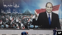 FILE - Workers clean the street under a billboard supporting Egyptian President Abdel Fattah el-Sissi for the presidential elections, in Cairo, Egypt, December 10, 2023.