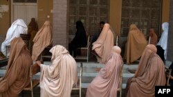Women wearing a burqa sit in a queue to collect financial assistance through the Ehsaas Emergency Cash programme for families in need, ahead of the Holy month of Ramadan in Peshawar on April 12, 2021. 