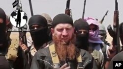 FILE - Omar al-Shishani standing next to Islamic State group spokesman among a group of fighters as they declare elimination of border between Iraq and Syria.