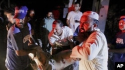 A Pakistani rescue worker and volunteers remove a body from the site of bomb explosion in Karachi, Pakistan, 11 Nov. 2010.