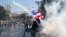 An anti-government protester throws back a tear gas canister fired by riot police in Bangkok, Thailand, Dec. 1, 2013.