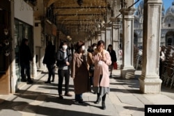 Tourists wearing protective masks walk through Saint Mark's Square in Venice, Italy, Feb. 27, 2020.