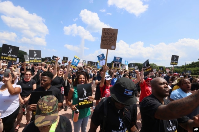 Striking screenwriters and actors hold signs at a rally in Chicago, Thursday, July 20, 2023, as the labor dispute that has halted Hollywood spreads to more cities. (AP Photo/Teresa Crawford)