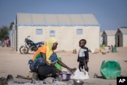 FILE - A displaced Burkinabe woman and child prepare food, in the Pissila town camp, near Kaya, Burkina Faso, Dec. 10, 2019.