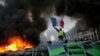 FILE - A demonstrator waves the French flag onto a burning barricade on the Champs-Elysees avenue during a demonstration against the rising of the fuel taxes, Nov. 24, 2018 in Paris.