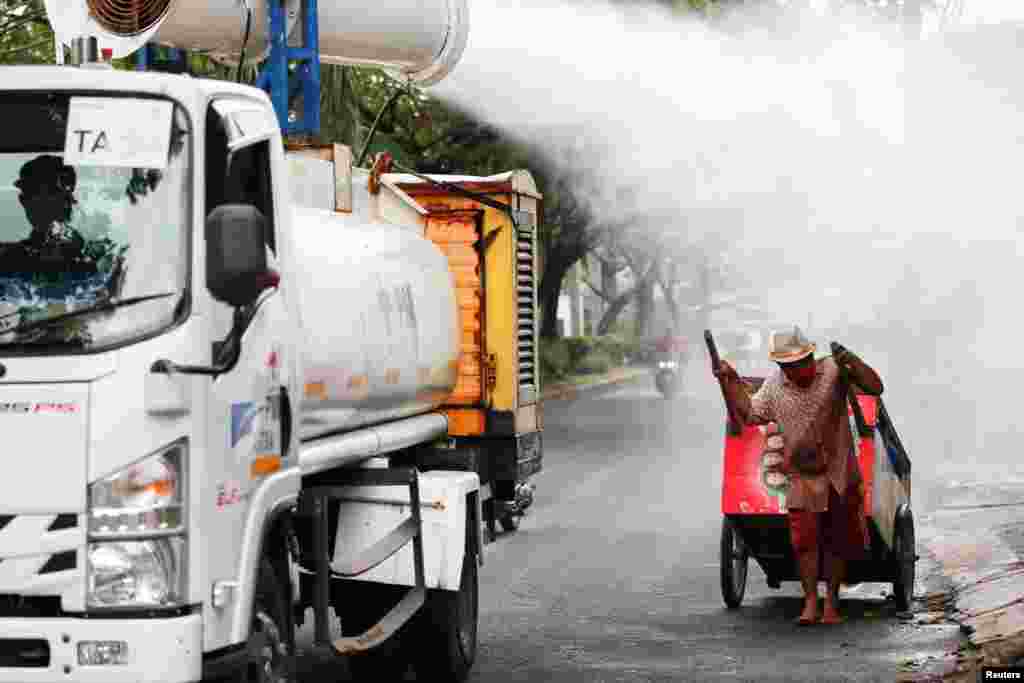 A man pulling a cart reacts as Indonesian Red Cross personnel spray disinfectant using a gunner, around the Daan Mogot neighborhood, as the number of COVID-19 cases surge in Jakarta, Indonesia.