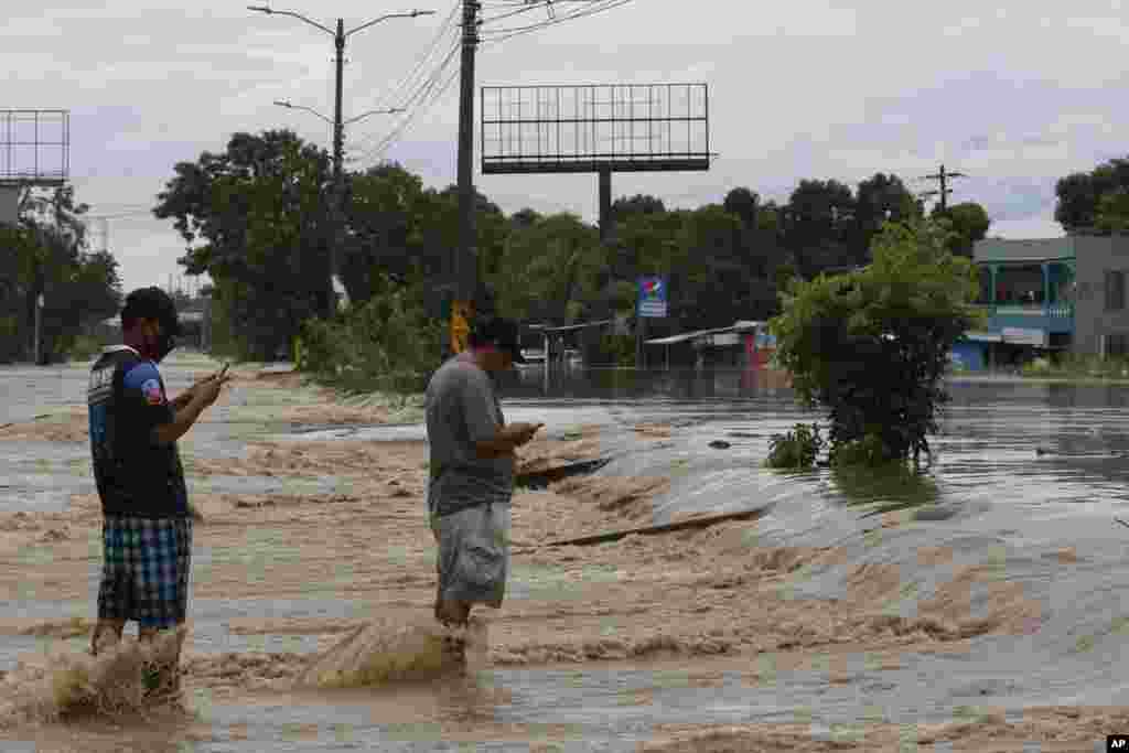 Men check their cell phones in the middle of a flooded street after the passing of Hurricane Iota in La Lima, Honduras.