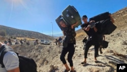 Syrians carry their luggage as they cross on foot into Syria through a crater caused by an Israeli airstrike to cut the road between the Lebanese and the Syrian checkpoints, at the Masnaa crossing, in the eastern Bekaa Valley, Lebanon, Oct. 4, 2024.