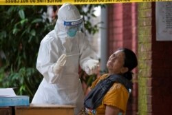 FILE - A woman reacts while getting a coronavirus swab test by medical staff at a quarantine center amid the COVID-19 outbreak in Yangon, Myanmar, Oct. 7, 2020.