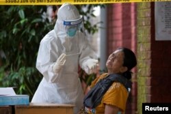 FILE - A woman reacts while getting a coronavirus swab test by medical staff at a quarantine center amid the COVID-19 outbreak in Yangon, Myanmar, Oct. 7, 2020.