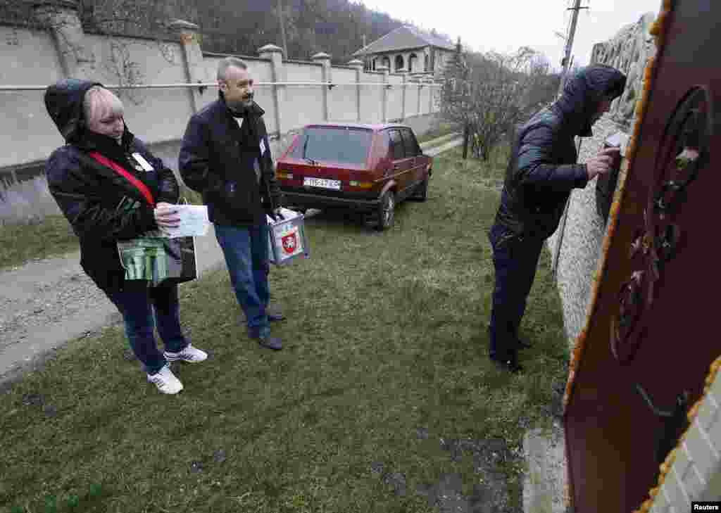 Membros da mesa de voto chegam a uma casa com as urnas móveis, para recolher o boletim de voto, para o Referendo na vila de Pionerskoye, Crimeia, Ucrânia, Março 16, 2014.