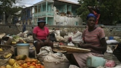 Women sell fruits and vegetables in front of a damaged house in Jacmel, Haiti.