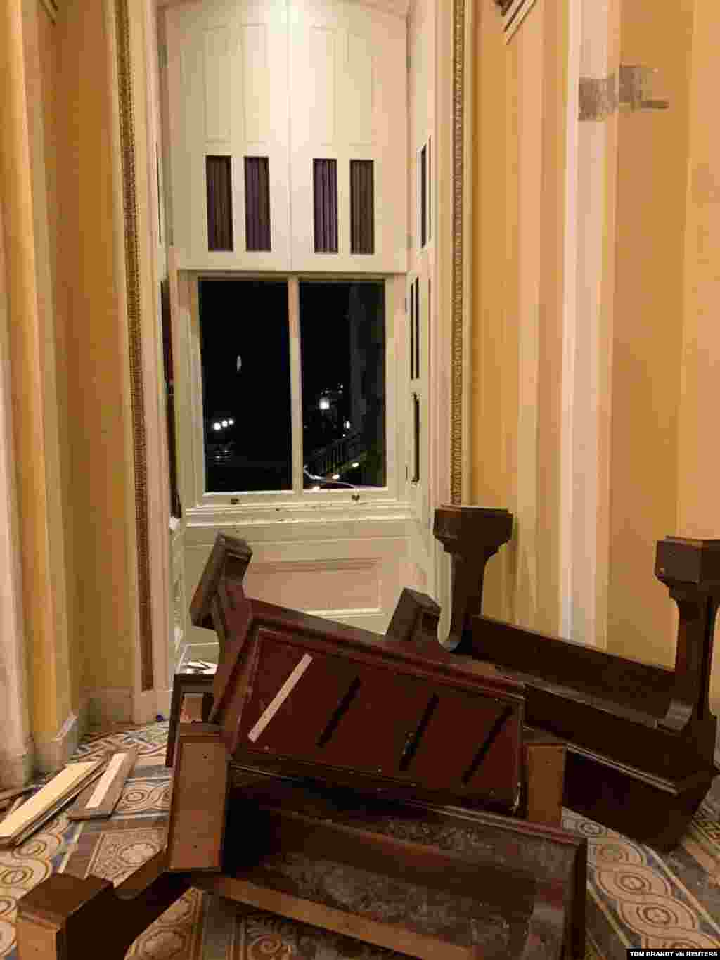  Muebles volteados y un vidrio de ventana roto yacen en el piso dentro del Capitolio.