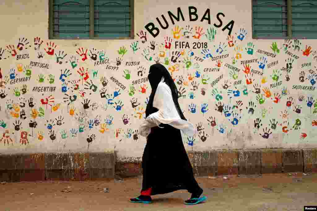 Seorang perempuan berjalan melewati dinding yang bergambar telapak tangan dan bertuliskan nama-nama negara menjelang turnamen Piala Dunia FIFA 2018 di Rusia. Mural tersebut dilukis oleh para penggemar sepak bola di sepanjang jalan Mombasa, di kawasan Lyari, di Karachi, Pakistan, 12 Juni 2018. (Foto: Reuters)