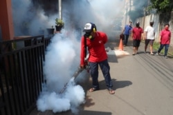 FILE - A worker fumigates a neighborhood in an effort to control the spread of dengue fever, amid the new coronavirus outbreak in Jakarta, Indonesia, May 17, 2020.