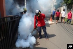 FILE - A worker fumigates a neighborhood in an effort to control the spread of dengue fever, amid the new coronavirus outbreak in Jakarta, Indonesia, May 17, 2020.