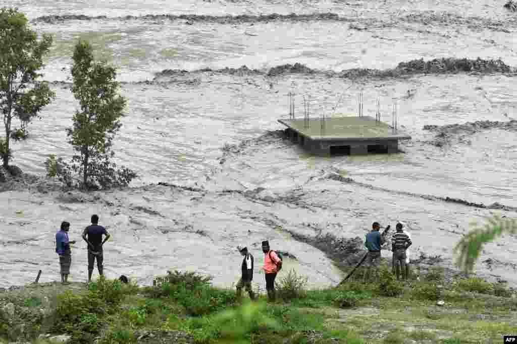 Residents stand along the banks of the overflowed Melamchi River following heavy monsoon rains in Sindhupalchok, some 70 km northeast of Kathmandu, Nepal.