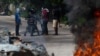 As bodies of alleged gang members burn in the foreground, local residents speak with a motorist in the street in Petion-Ville, a suburb of Port-au-Prince, Haiti, Nov. 19, 2024.