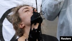 A man pours fake fuel on the face of a protester as they perform at a demonstration against the fossil fuel industry during the U.N. Climate Change Conference (COP26), in Glasgow, Scotland.