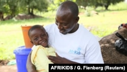 FILE - Joseph Asakibeem, project manager with charity AfriKids and winner of the Bond Humanitarian Award 2018 for his work with disabled children, hugs a child, Richmond, in Ghana's Upper East Region, Sept. 2014..