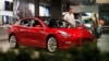 FILE- In this July 6, 2018, file photo, a prospective customer confer with sales associate as a Model 3 sits on display in a Tesla showroom in the Cherry Creek Mall in Denver.