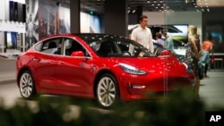 FILE- In this July 6, 2018, file photo, a prospective customer confer with sales associate as a Model 3 sits on display in a Tesla showroom in the Cherry Creek Mall in Denver.