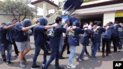 FILE - Police officers escort men arrested in a raid on a gay sauna at North Jakarta police headquarters in Jakarta, Indonesia, May 22, 2017. 