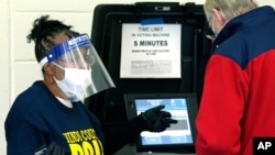 Precinct 36 poll worker Vivian Bibens in her personal protective equipment explains the purpose of the ballot scanner to a voter on Election Day in Jackson, Miss., Nov. 3, 2020.
