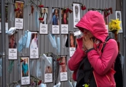 FILE - A woman reacts as she walks past photos of St. Petersburg's medical workers who died from the coronavirus after being infected at work, at a makeshift memorial at a local health department in St. Petersburg, Russia, May 20, 2020.