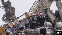 FILE - After a brief stop to demolish the standing debris, search and rescue personnel continue to work in the rain on the rubble pile of the 12-story Champlain Towers South condo that partially collapsed on July 5, 2021 in Surfside, Florida. 