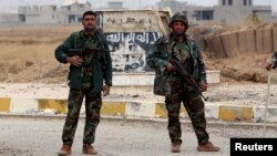 FILE - Kurdish Peshmerga fighters stand in a street against the backdrop of a defaced Islamic State flag in the town of Sinjar, northern Iraq, Nov. 16, 2015.