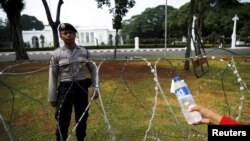 FILE - An Indonesian street vendor offers water to a policeman as he guards in front of the Presidential Palace in Jakarta, Oct. 15, 2015. 