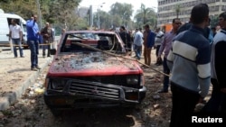 People stand near a damaged car after explosions near Cairo University, April 2, 2014. 