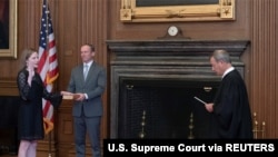 U.S. Supreme Court Chief Justice John Roberts administers the judicial oath of office to Judge Amy Coney Barrett as Judge Barrett’s husband Jesse Barrett holds the Bible in the East Conference Room of the Supreme Court Building in Washington.