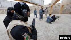 A German police officer guards an Afghan National Police trainee as she fires her weapon at a training center in Mazar-e-Sharif, northern Afghanistan, December 18, 2012. 