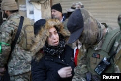 A woman reacts near fighters of Hayat Tahrir al-Sham during what HTS said were security checks to find "remnants" of ousted Syrian President Bashar al-Assad's force, in Wadi al-Dahab neighborhood in Homs, Syria, Jan. 2, 2025.