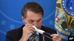 Brazil's President Jair Bolsonaro puts on a mask during a news conference on the new coronavirus at the Planalto Presidential Palace in Brasilia, Brazil, March 18, 2019. 